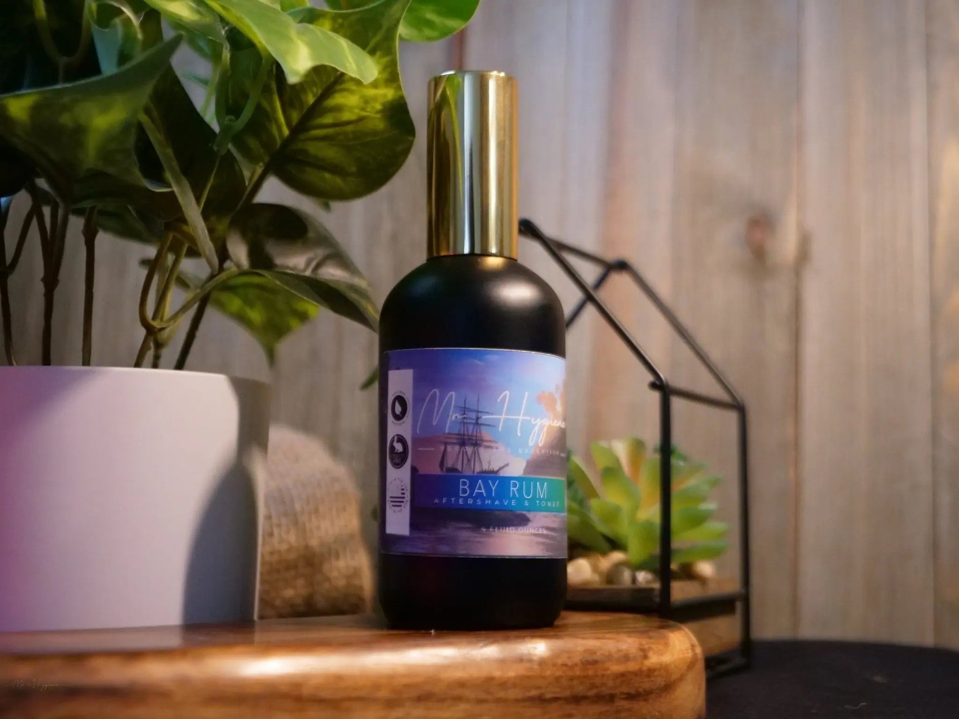 Bay Rum Aftershave bottle displayed on a wooden surface with decorative plants
