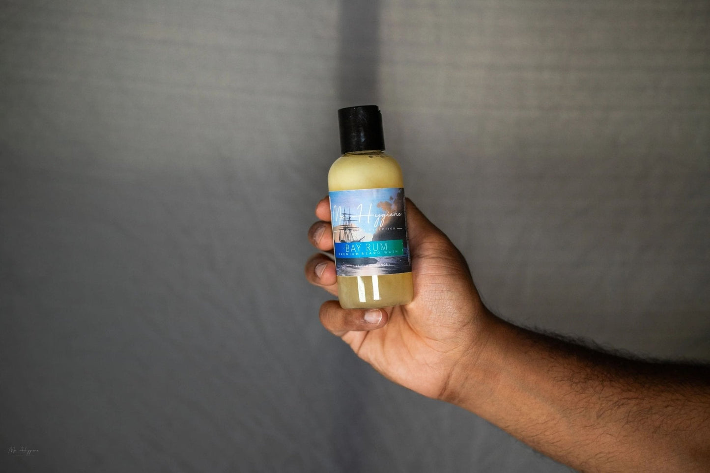 Hand holding Bay Rum Beard Wash – Bold Scent, Clean Beard Routine bottle against gray background