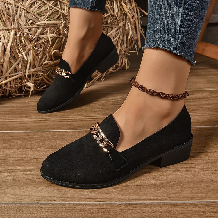 Black loafers with chain detail on women's feet, wooden floor background