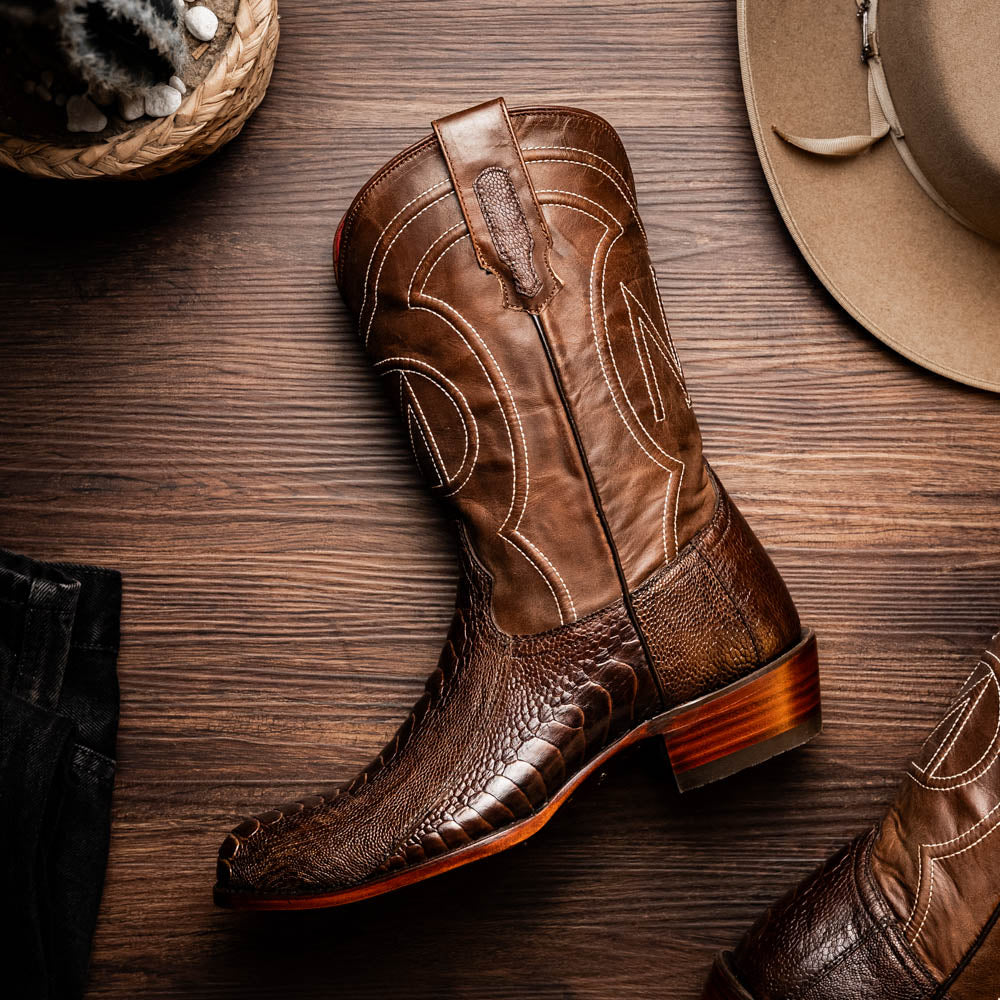 Denver Clear Brown genuine ostrich leg skin cowboy boot from Western Collection on wooden floor with cowboy hat and woven basket.