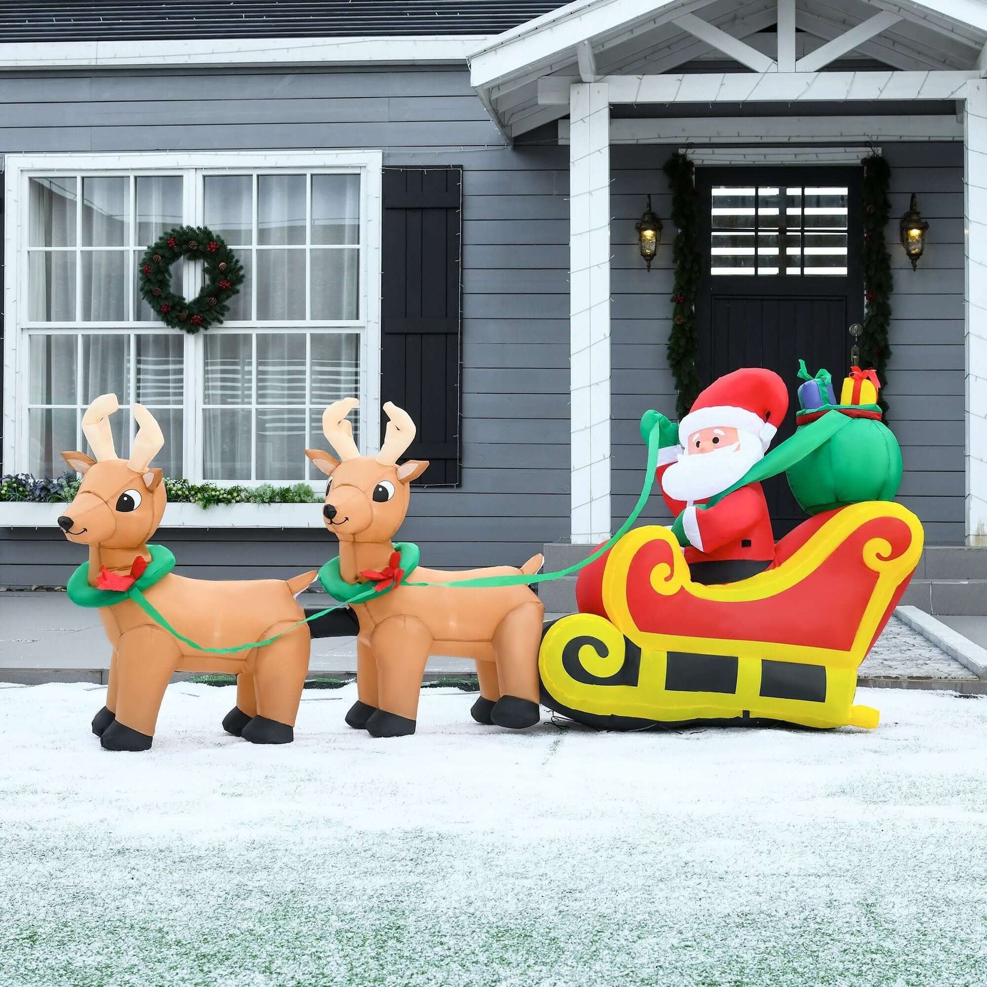 Christmas Inflatable Santa Claus with Sleigh and reindeer by a house, featuring LED lights for festive outdoor decoration.