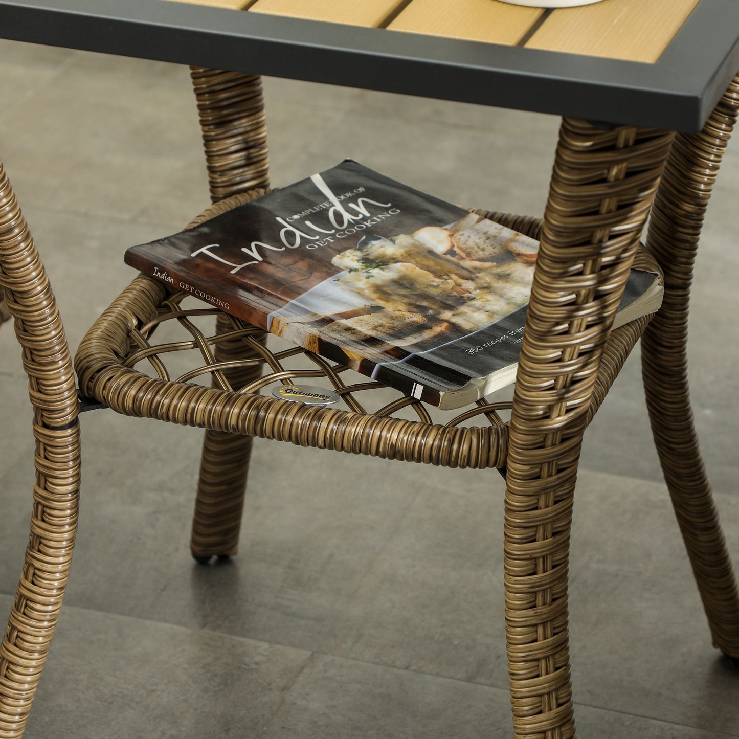 Wicker table from Outsunny 3 Piece Outdoor Bistro Set with a magazine on the lower shelf, showcasing durable and stylish patio furniture.