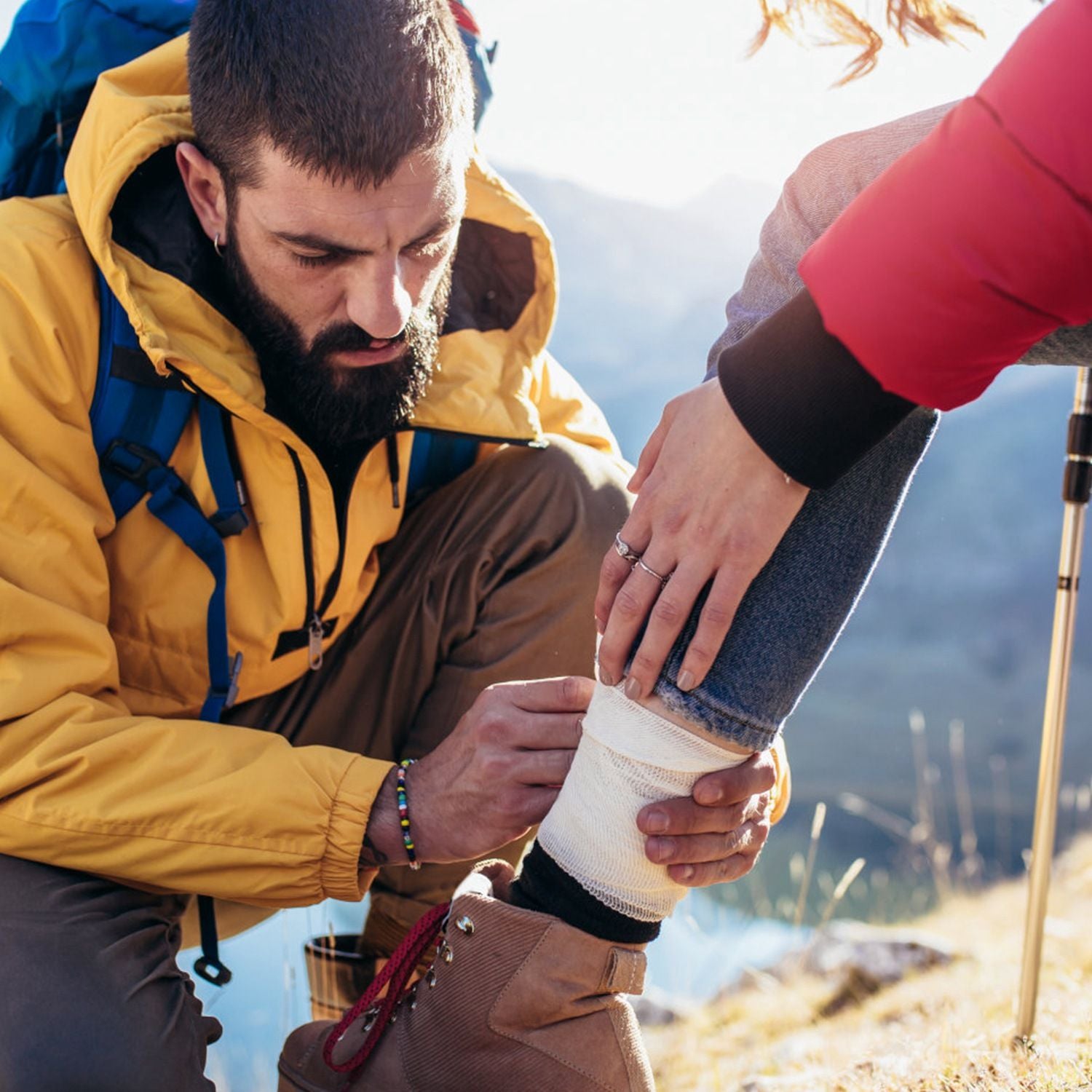 Adventurer using 125Pcs Survival Kit to bandage an ankle during outdoor hiking trip, showcasing its first aid capabilities. Ideal for emergency use.