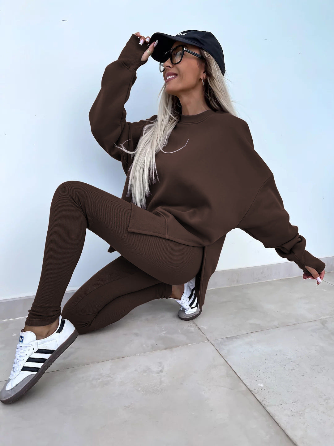 Woman wearing Women’s Casual Sweater Suit – Loose Split Top & Fitted Trousers Set, brown color, casual pose with cap and sneakers.