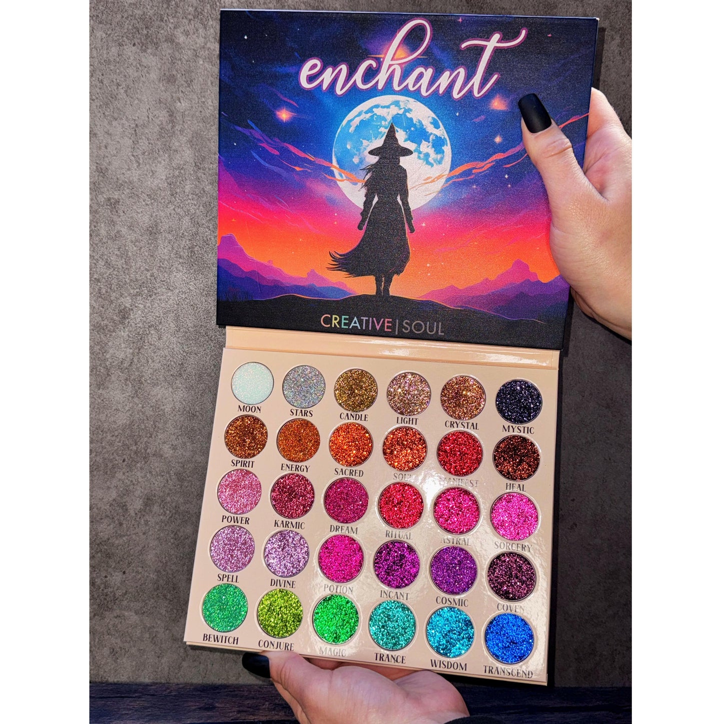 Enchant Pressed Glitter Eyeshadow Palette with 30 vibrant shades including iridescent, golds, purples, and blues for a magical look.