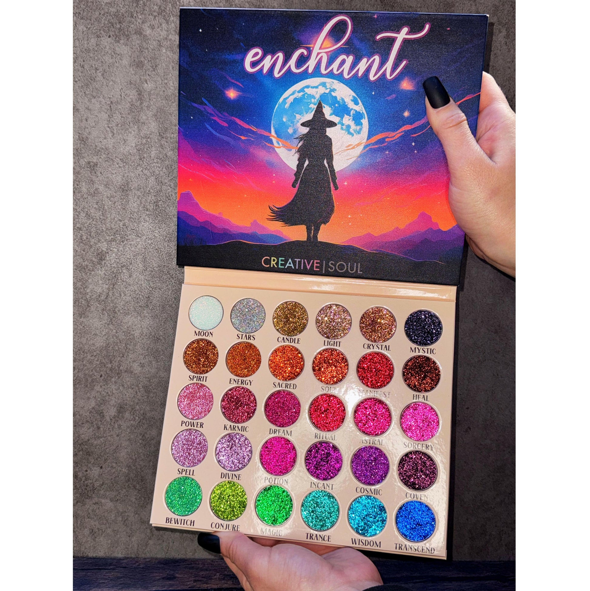 Enchant Pressed Glitter Eyeshadow Palette with 30 vibrant shades including iridescent, golds, purples, and blues for a magical look.