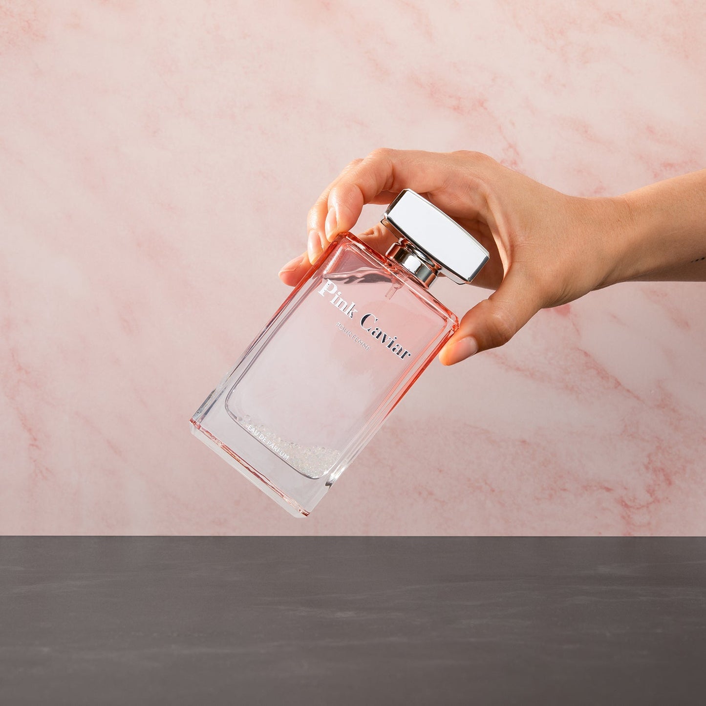 Hand holding Syren - Pink Caviar perfume bottle against a pink background.