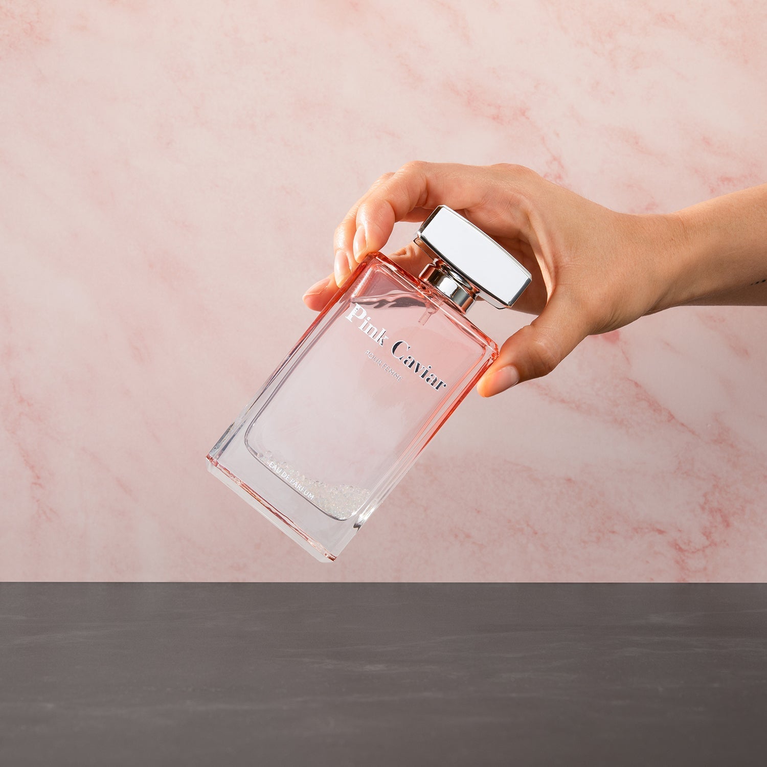 Hand holding Syren - Pink Caviar perfume bottle against a pink background.