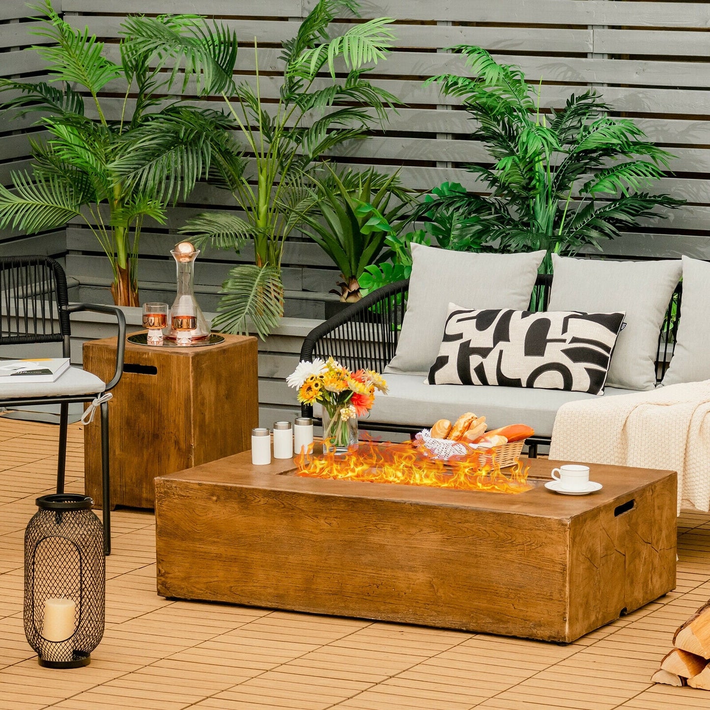 2 Piece Outdoor Propane Fire Pit Table Set with tank holder and lava rocks on a patio with plants and seating