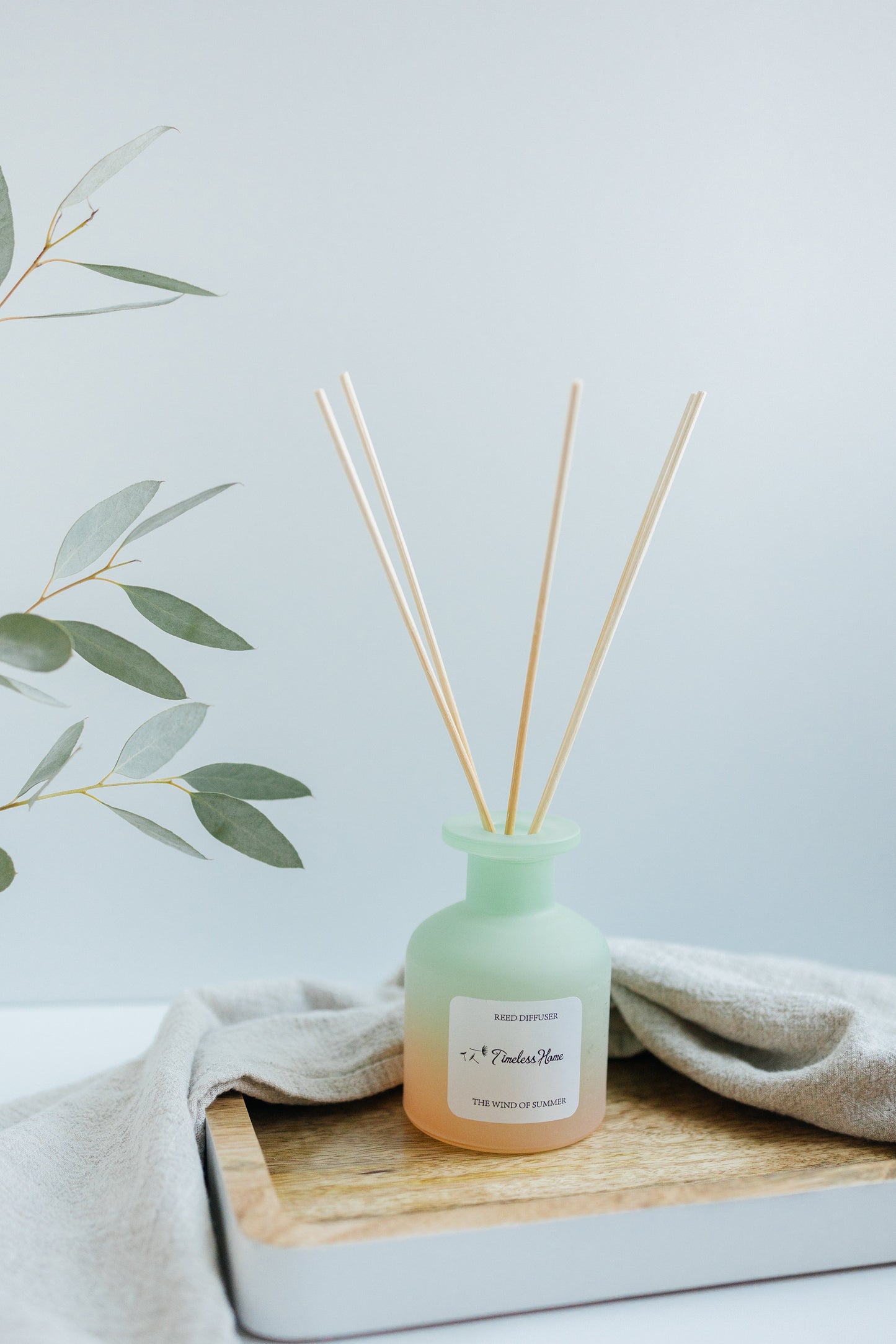 Reed Diffuser - The Wind of Summer in a frosted glass vessel with natural reed sticks on a wooden tray.