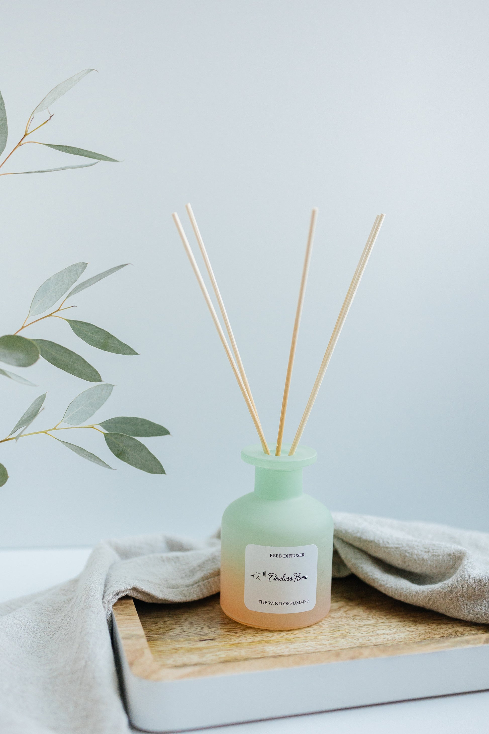 Reed Diffuser - The Wind of Summer in a frosted glass vessel with natural reed sticks on a wooden tray.