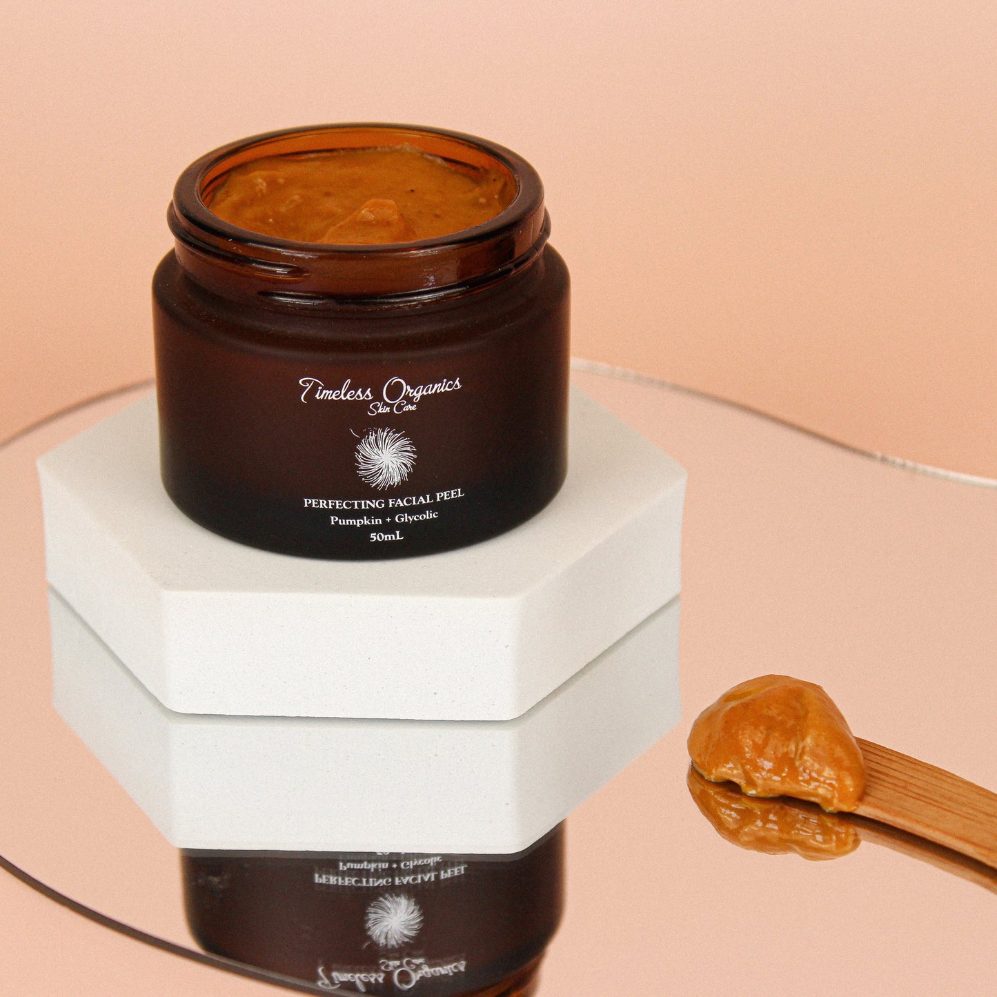 Pumpkin + Glycolic Facial Peel in amber jar with natural exfoliating formula on a spatula, ideal for brightening and renewing skin.