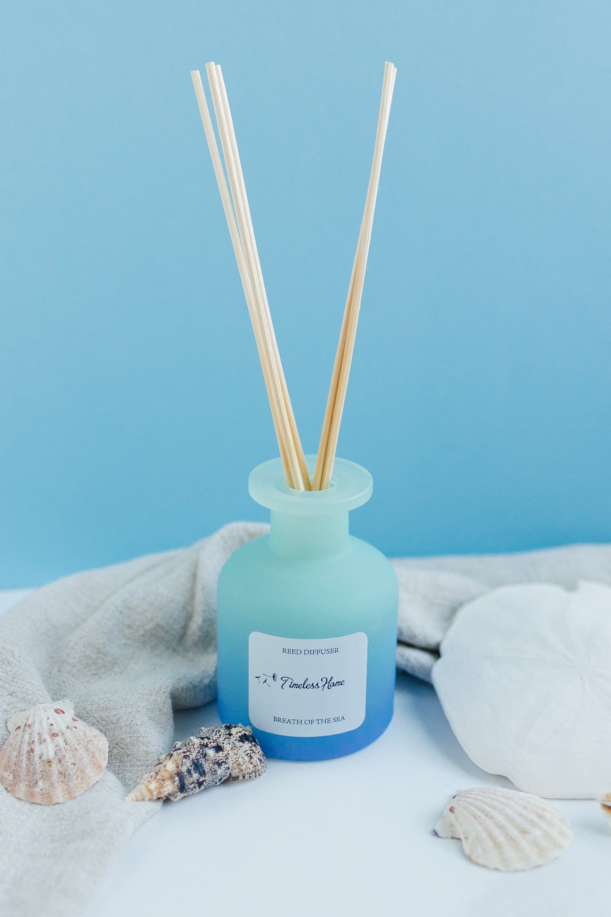 Reed Diffuser - Breathe of The Sea with ocean-inspired notes in a frosted glass vessel, surrounded by seashells on a blue backdrop.
