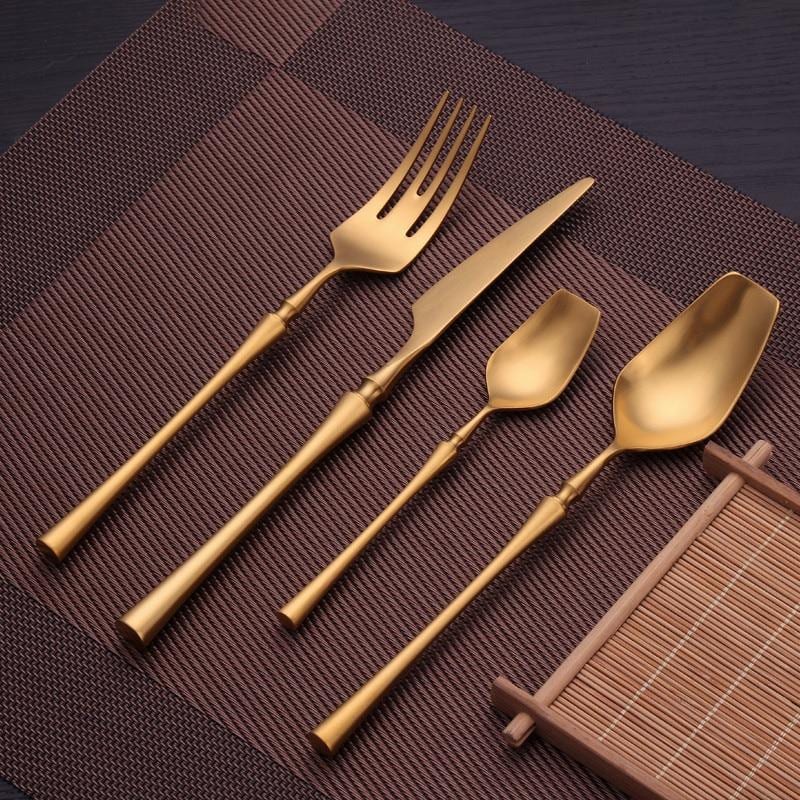 Evangeline Matte Flatware Set 24-Piece in gold with modern skeleton shapes on a placemat.