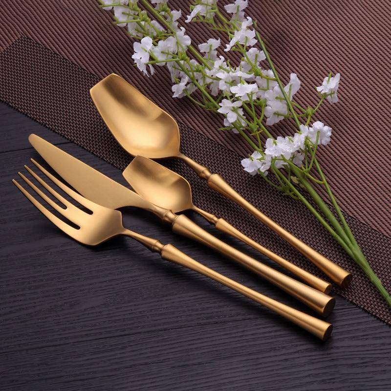 Evangeline Matte Flatware Set 24-Piece in modern matte gold finish displayed with white flowers on a dark dining table.