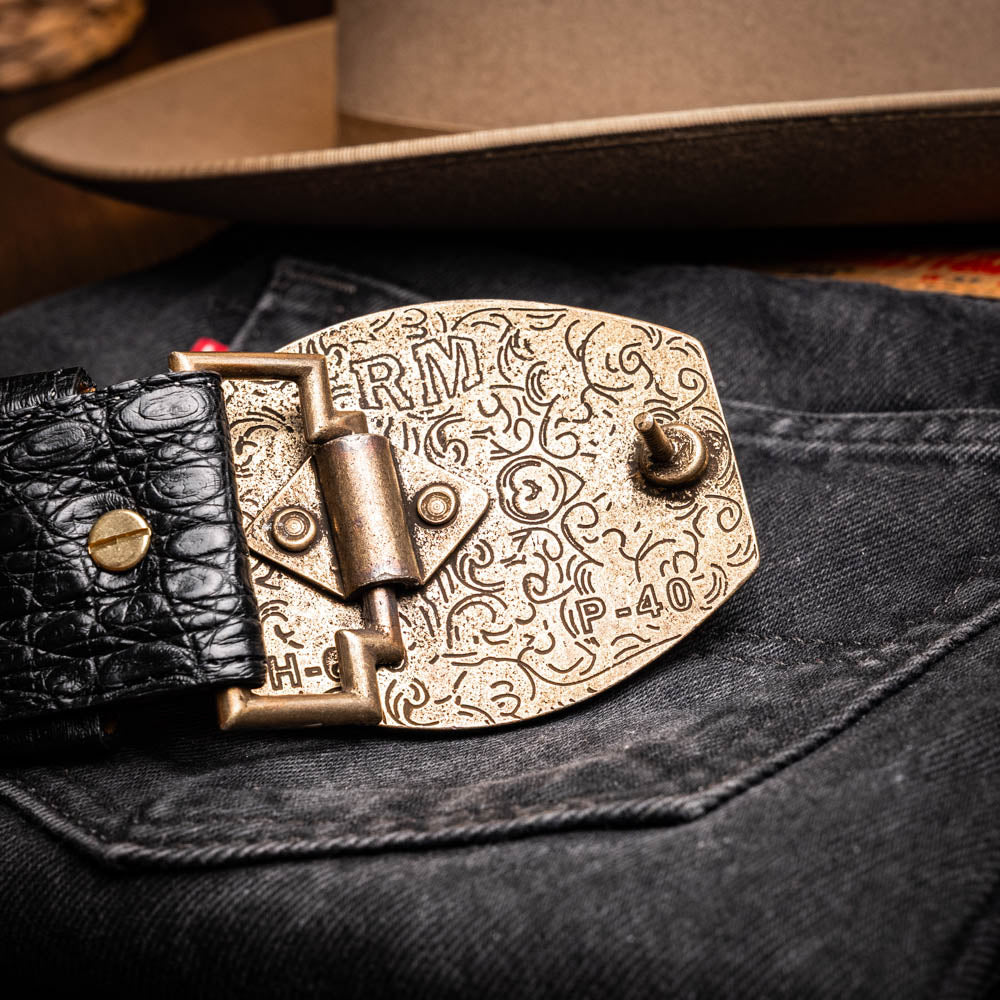 Iowa Belt Black with antique brass buckle and genuine caiman skin resting on denim jeans, showcasing Western craftsmanship.