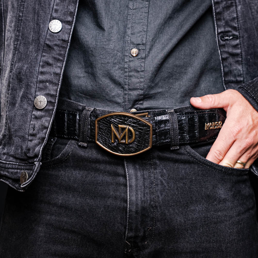Man wearing Iowa Belt Black made from genuine caiman crocodile skin with a Western-style brass buckle, showcasing artisanal detailing.