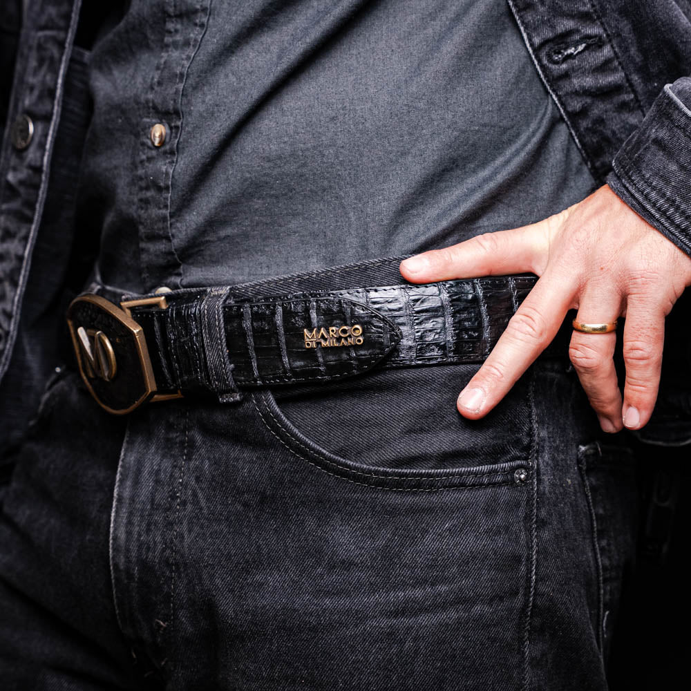Close-up of Iowa Belt Black in genuine caiman skin with antique brass buckle, worn with black denim outfit.