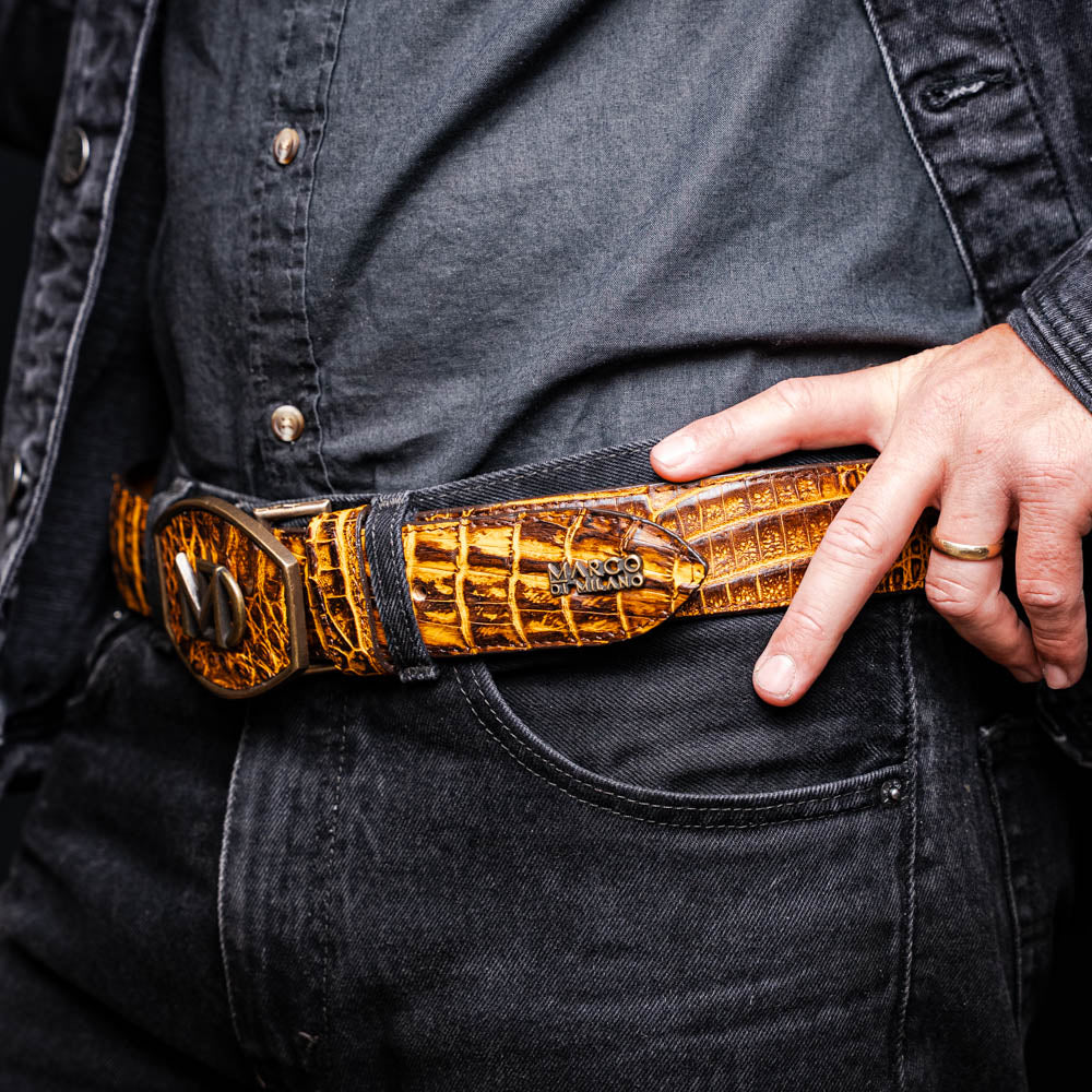 Iowa Belt Mustard Brown made of genuine caiman skin with antique brass buckle showcased on a person wearing black denim.