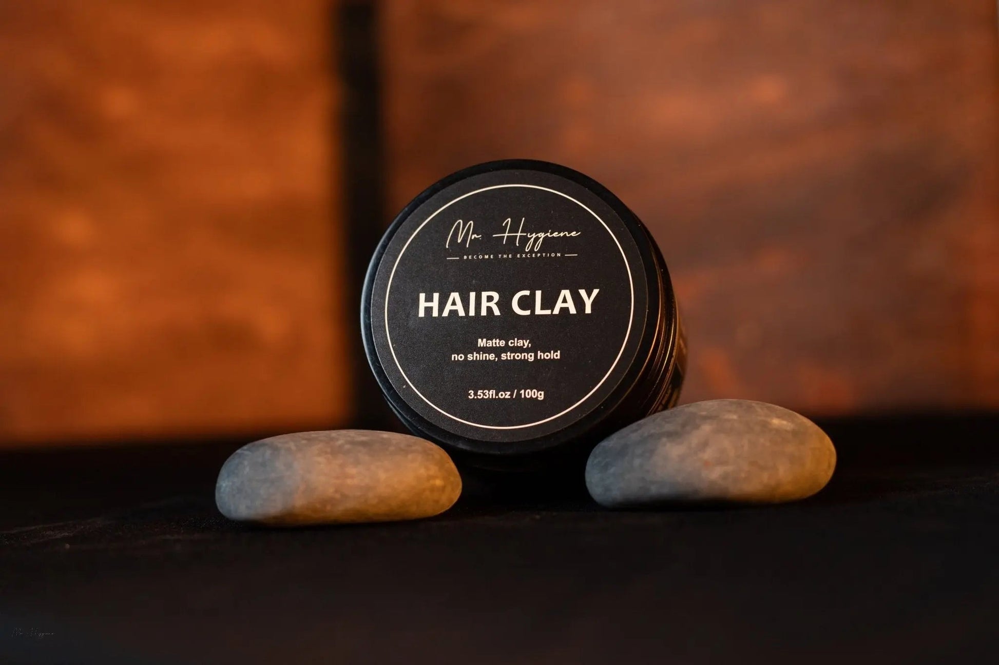 Matte Finish Hair Clay - Strong Hold. Zero Shine. All-Day Control. in stylish black packaging surrounded by stones.
