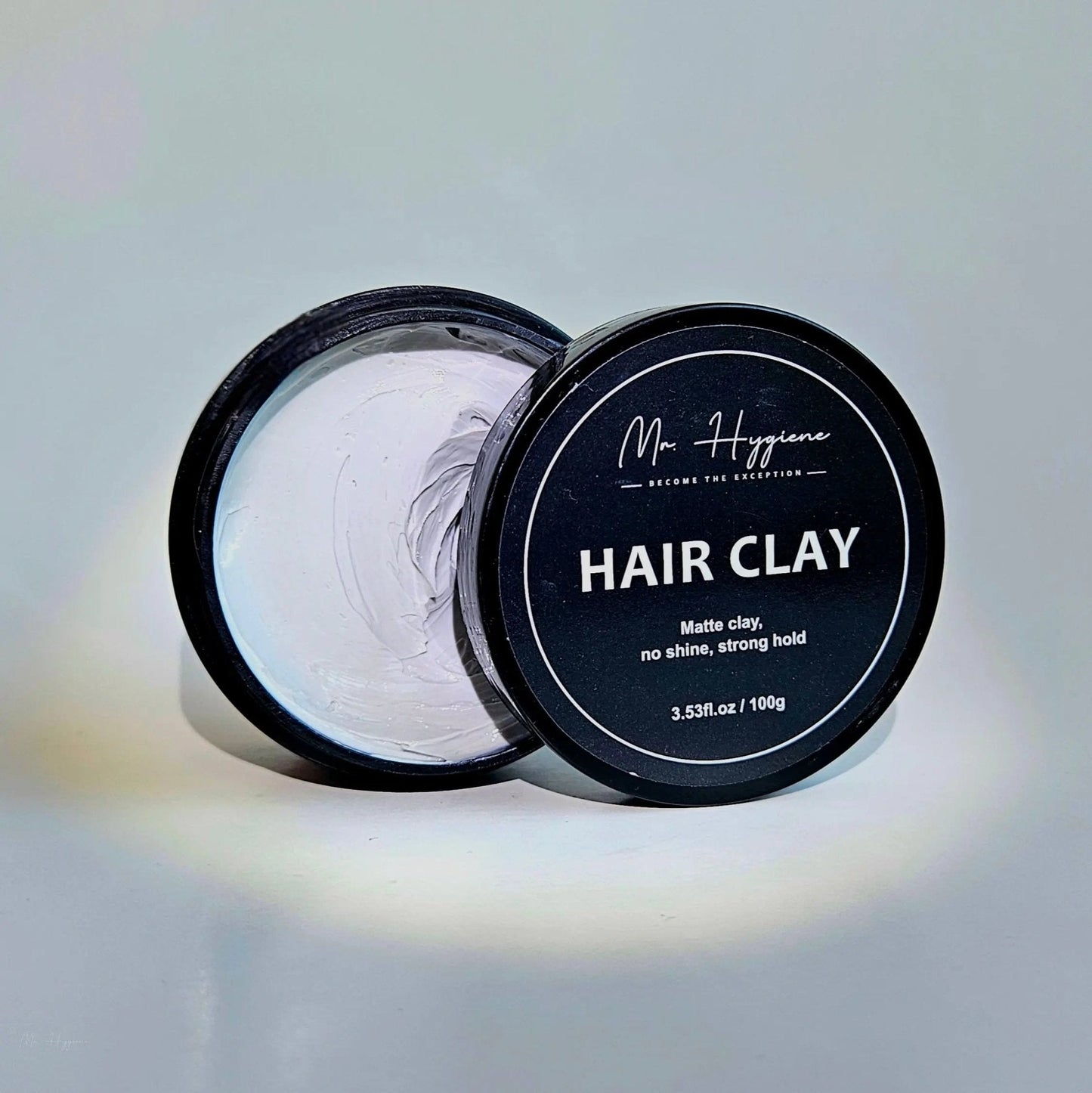 Matte Finish Hair Clay - Strong Hold. Zero Shine. All-Day Control. Open black container with clay on a light background.
