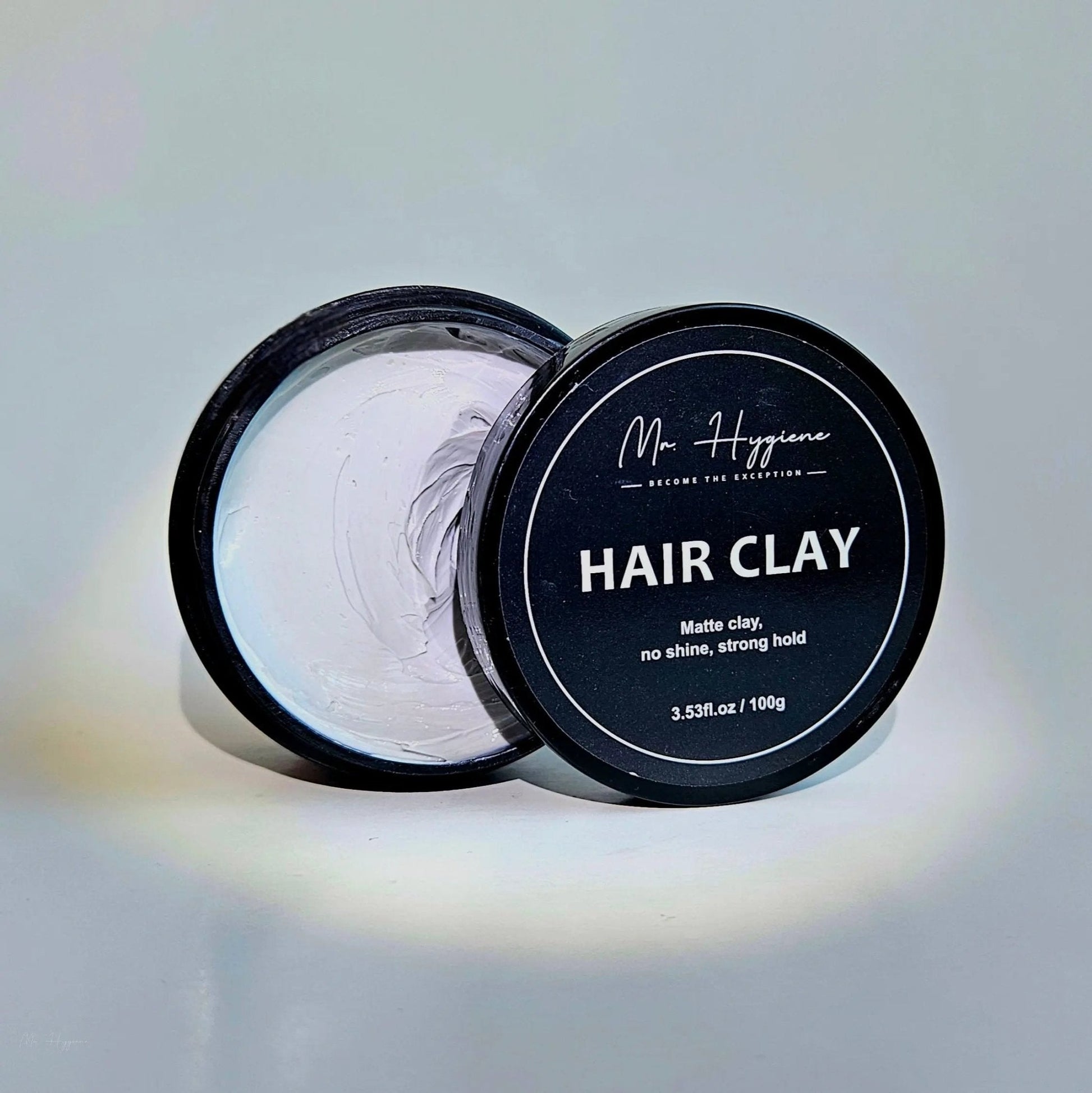 Matte Finish Hair Clay - Strong Hold. Zero Shine. All-Day Control. Open black container with clay on a light background.