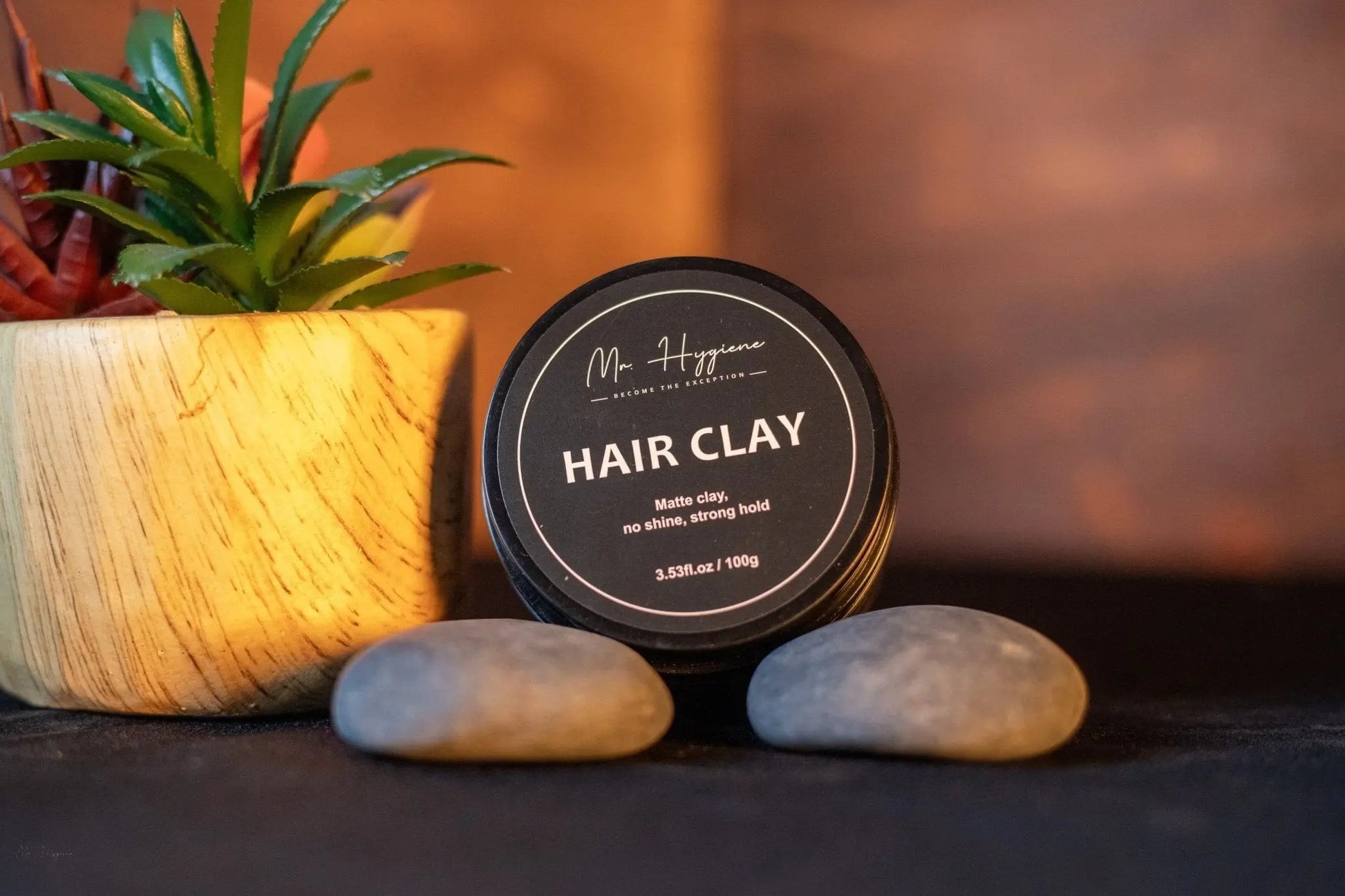 Matte Finish Hair Clay - Strong Hold. Zero Shine. All-Day Control. next to a plant and stones on a dark surface.