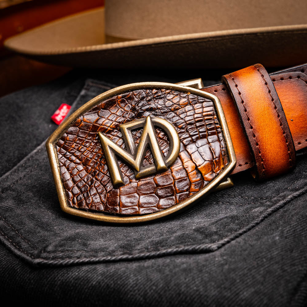 Montana Belt Aged Brown with MD logo, featuring caiman and calfskin leather, resting on denim jeans with cowboy hat in background.