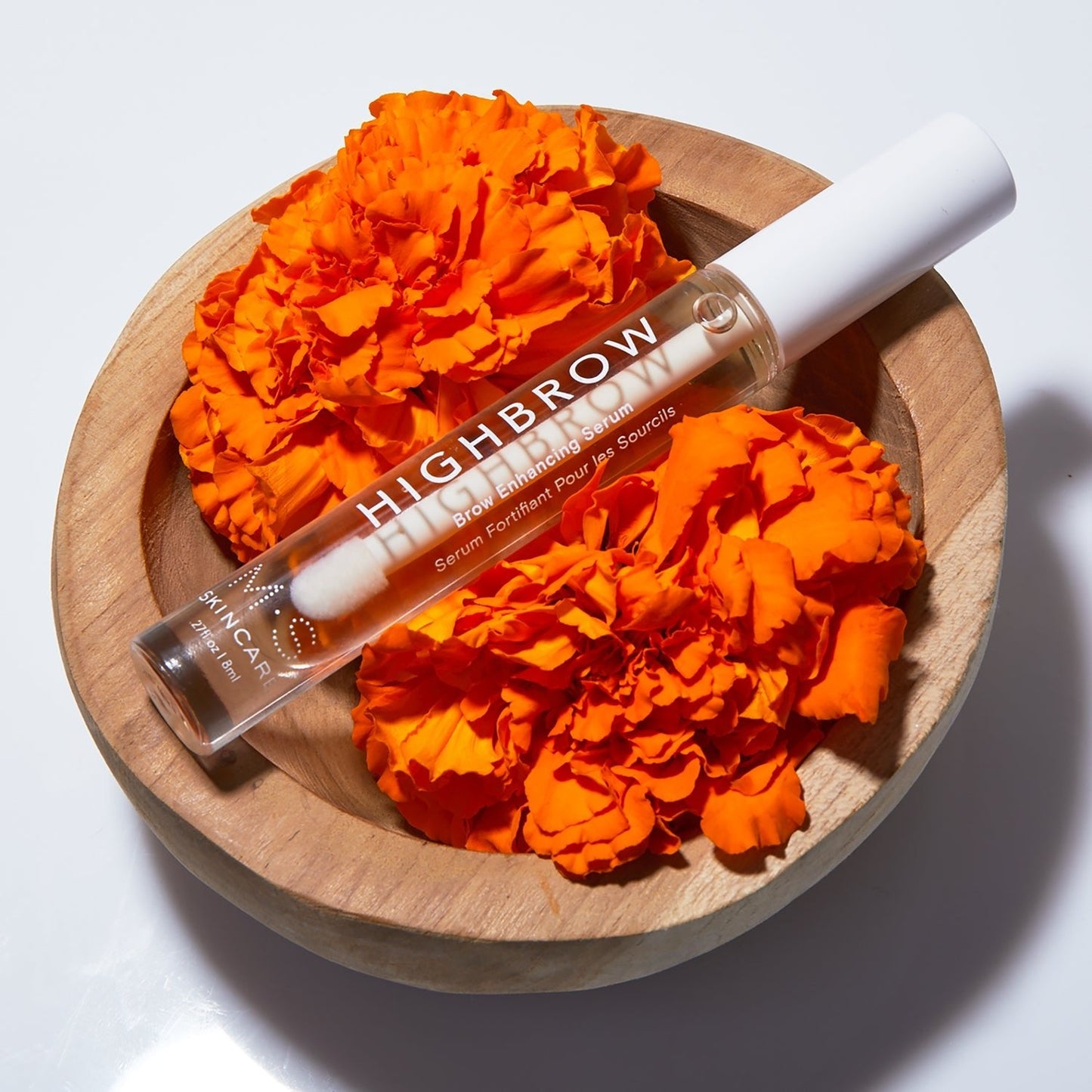 HIGHBROW nourishing serum with Ayurvedic oils for stronger, fuller brows displayed with orange flowers