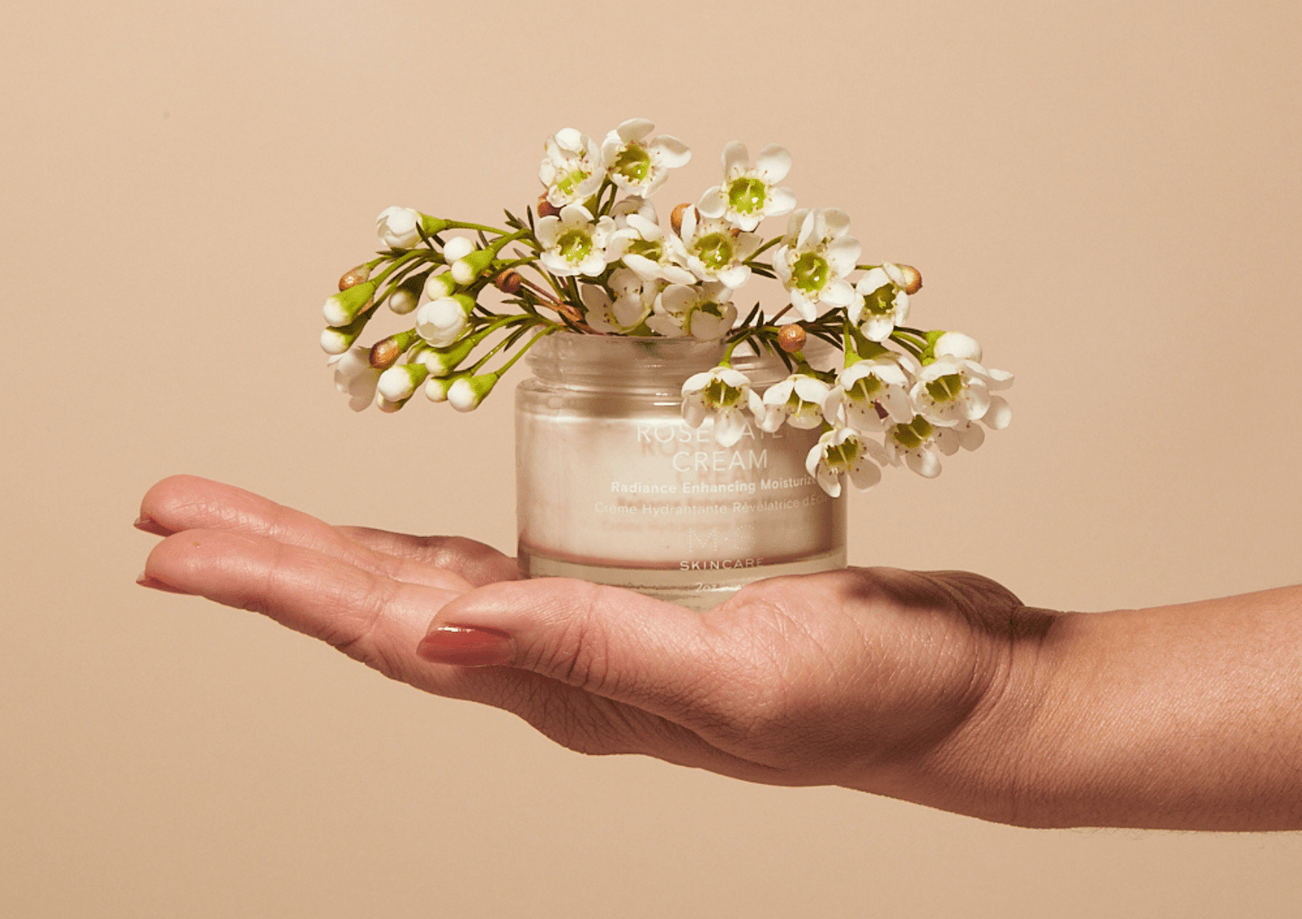 ROSEWATER CREAM jar held in hand with white flowers, featuring Ayurvedic oils and organic extracts for radiant skin