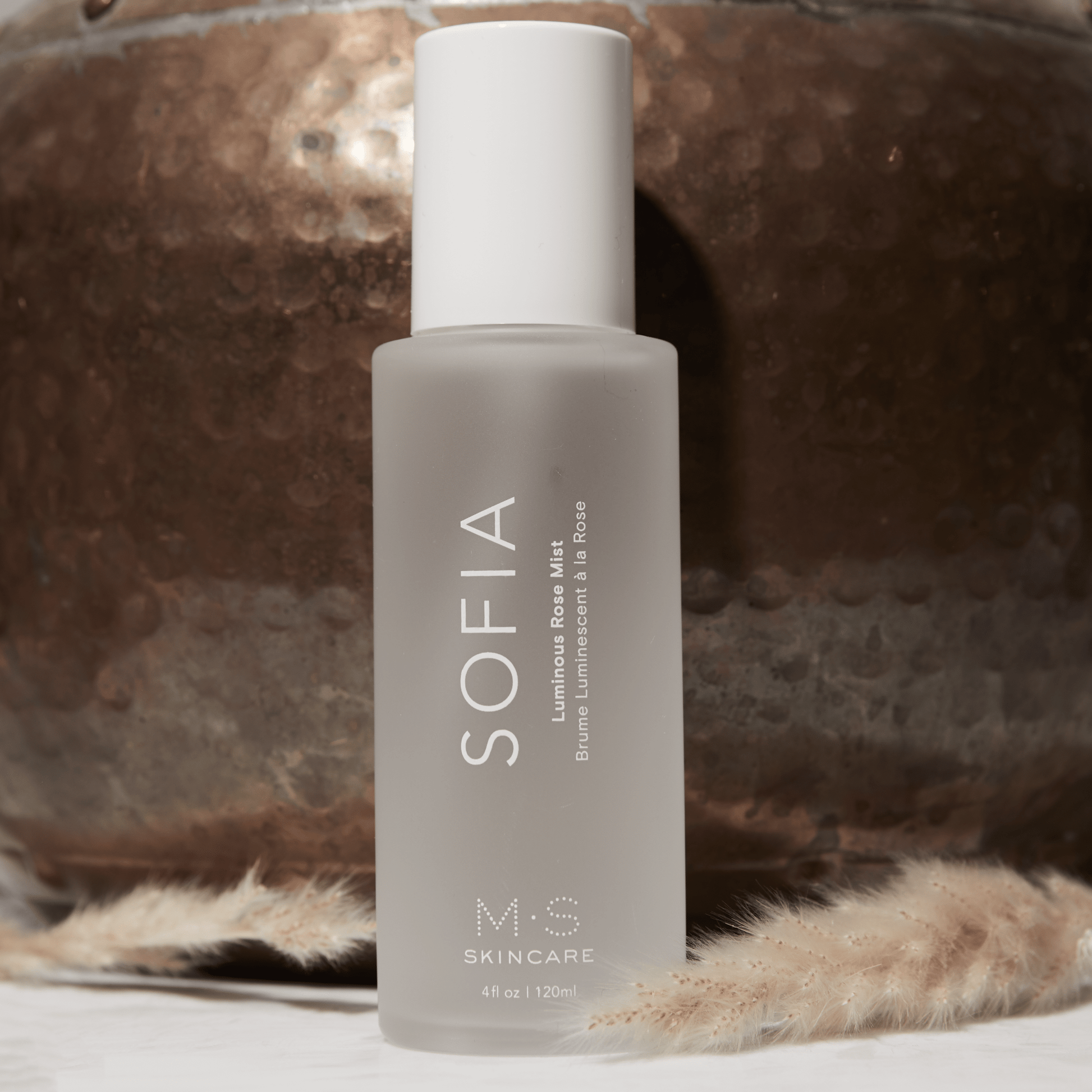 SOFIA Luminous Rose Mist bottle on rustic background, 4 fl oz / 120 ml, featuring antioxidants for radiant skin.