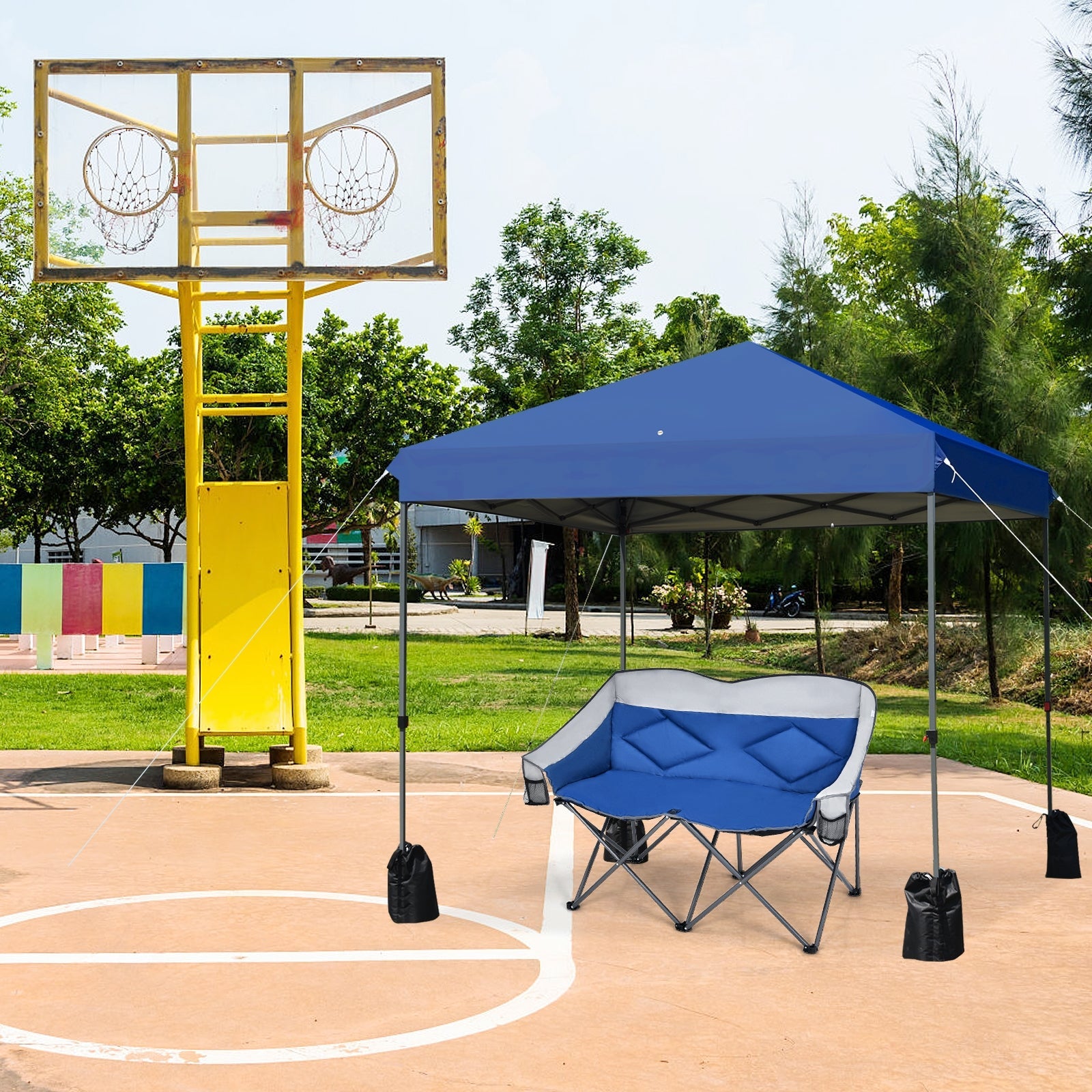 8x8 Pop Up Canopy Tent w/Roller Bag-Blue set up next to a basketball court with trees in the background.