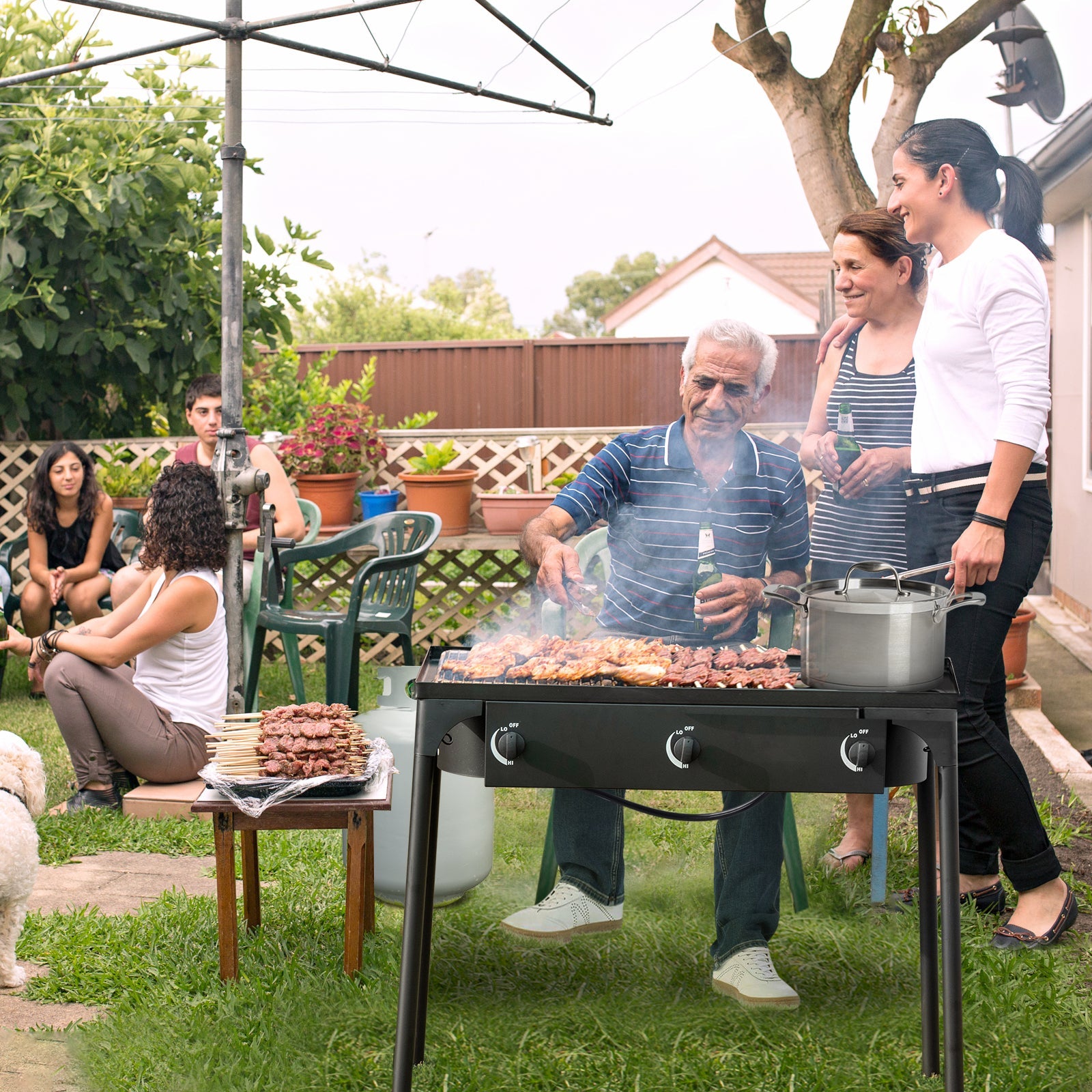 Outdoor barbecue using 225000 BTU Portable Propane 3 Burner Gas Cooker in a garden with people enjoying a meal.