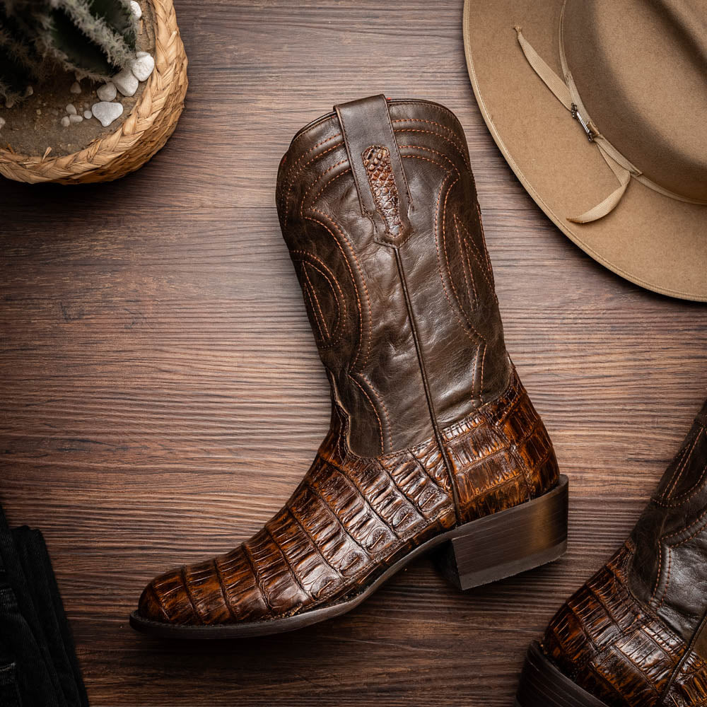 Phoenix Aged Brown cowboy boot made of genuine caiman belly skin with full-grain leather shaft on a wooden floor background.
