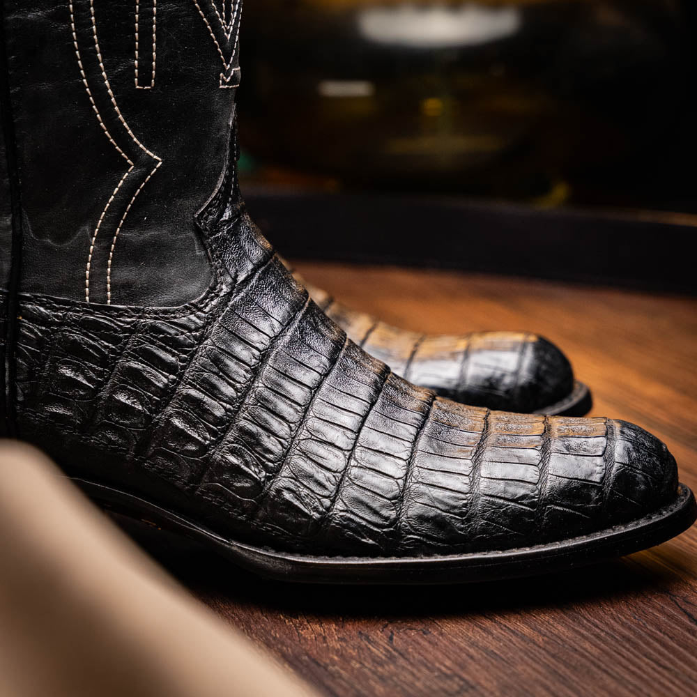 Phoenix Black cowboy boot with genuine caiman belly skin and polished finish, part of the Western Collection, on a wooden surface.