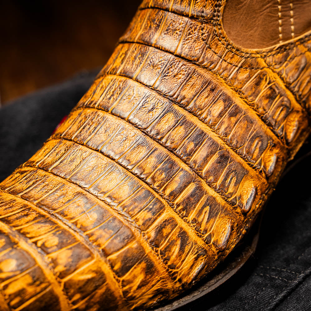 Close-up of Phoenix Mustard Brown cowboy boot crafted with genuine caiman belly skin, showcasing a smooth texture and scale pattern.