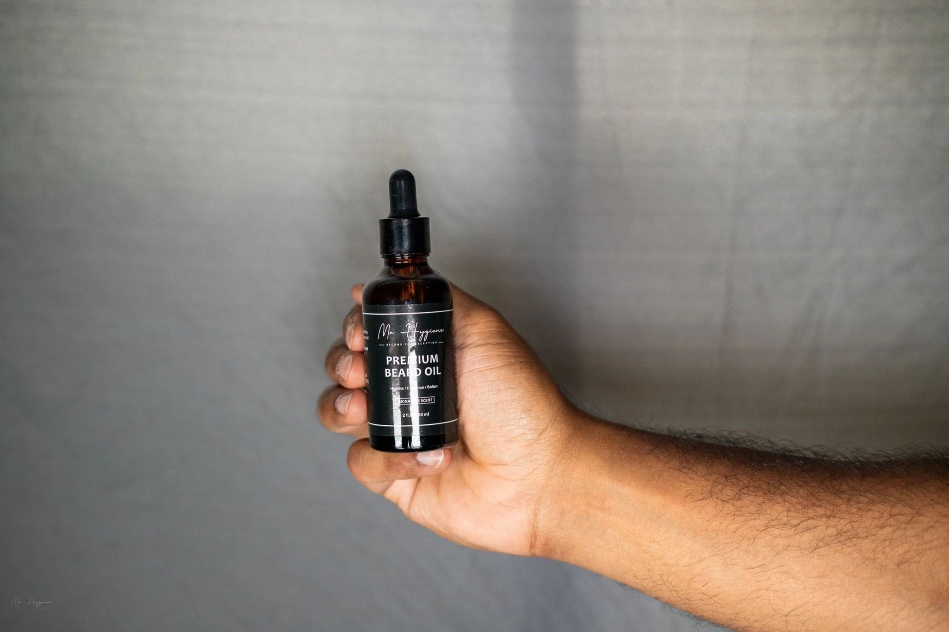 Hand holding Mr. Hygiene's Premium Beard Oil bottle from the Premium Beard Oil and Balm Set against a neutral background.
