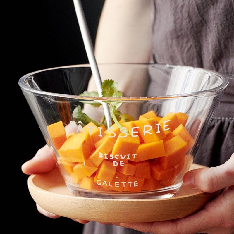 French Letter Glass Bowl filled with diced vegetables, held by a person in front of a dark background.