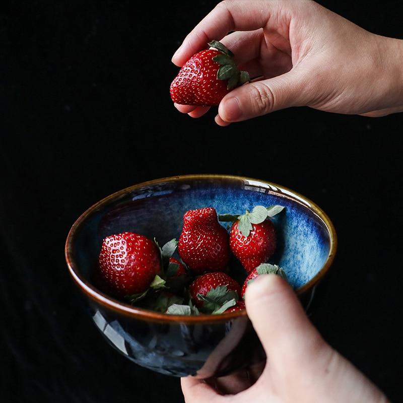 Person holding an Eye Of Cat Bowl with fresh strawberries, showcasing ceramic glaze technique and eco-friendly material.