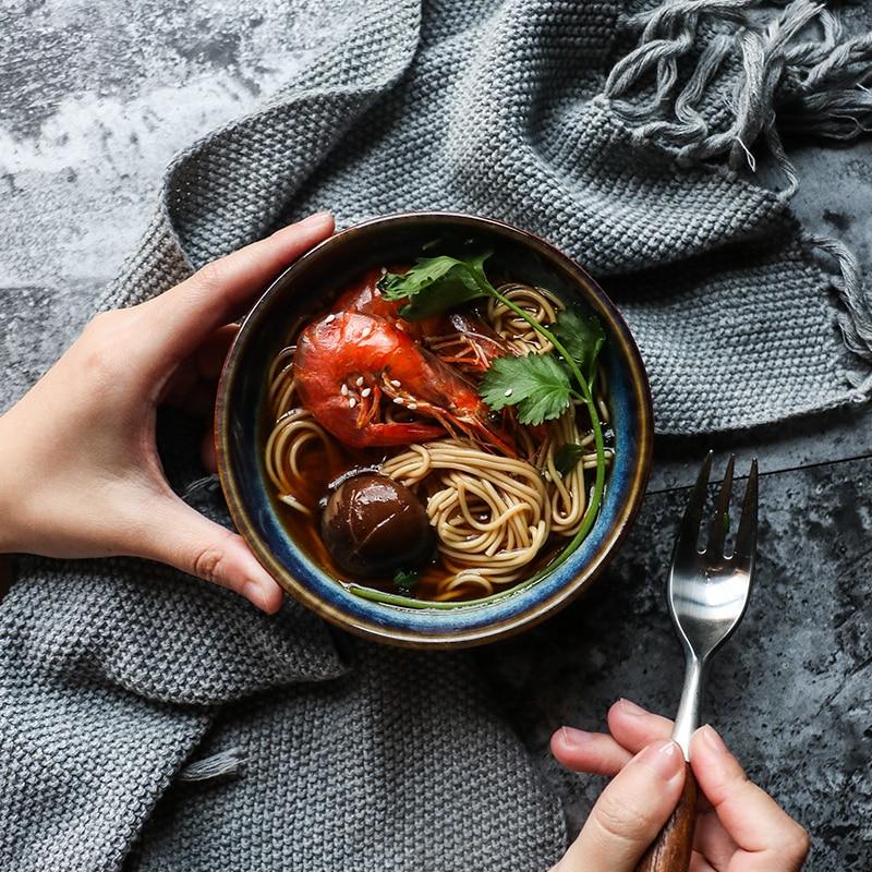 Person holding an Eco-Friendly ceramic Eye Of Cat Bowl with ramen and shrimp on a textured surface.
