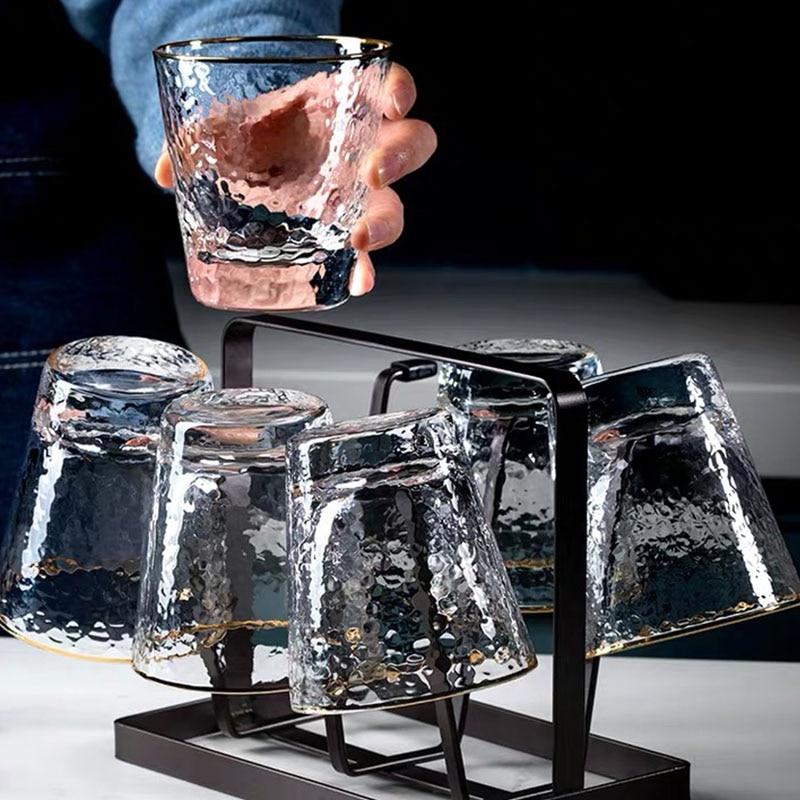 Hand holding a Golden Rim Clear Whiskey & Water Glass placed on a glass rack, showcasing modern and elegant design for home use.