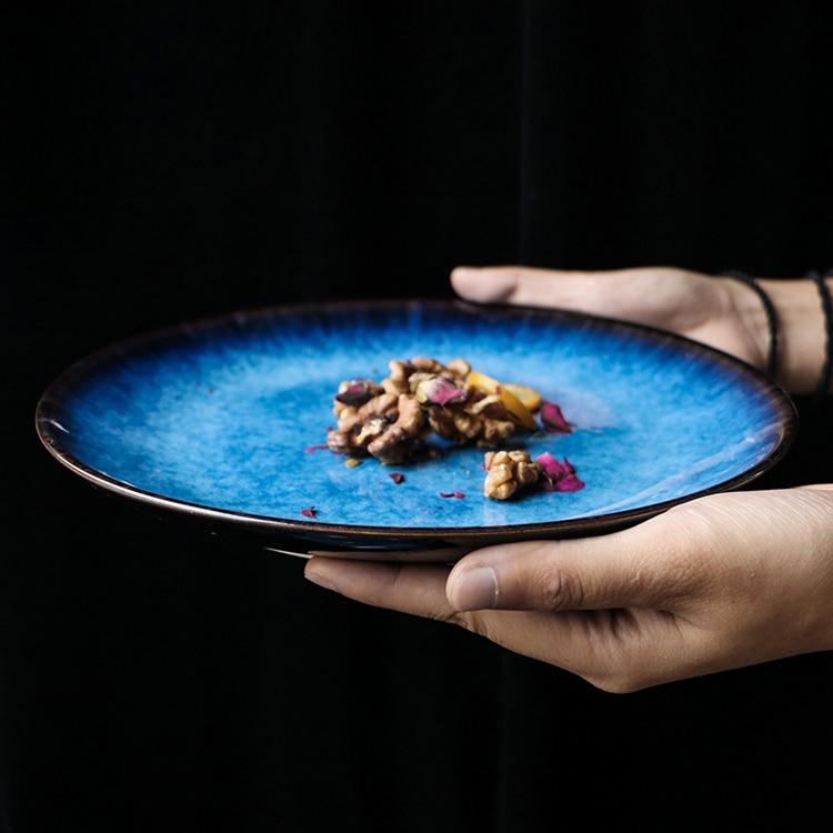 Hand holding blue ceramic dish from Pallas Plate Set Of 4 with decorative food, displaying unique handpainted design.