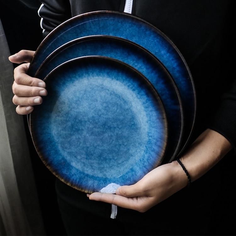 Person holding Pallas Plate Set Of 4, round handpainted ceramic plates with blue glaze, showcasing minimalist design.