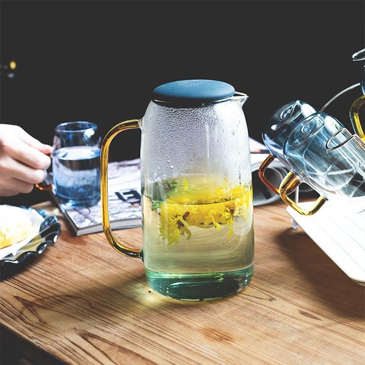 Colored Glass Carafe and Glass Set on wooden table with transparent eco-friendly glassware and floral tea.