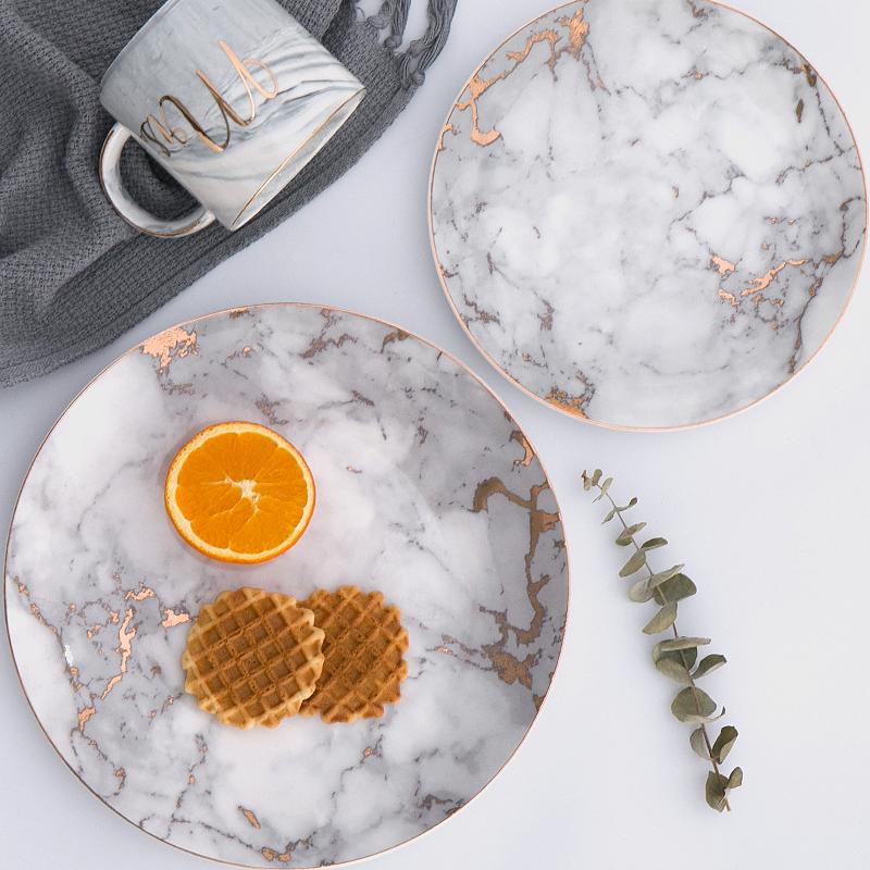 Selene Plates on display with two marbled ceramic plates, a mug, and decorative elements, showcasing elegant design and craftsmanship.