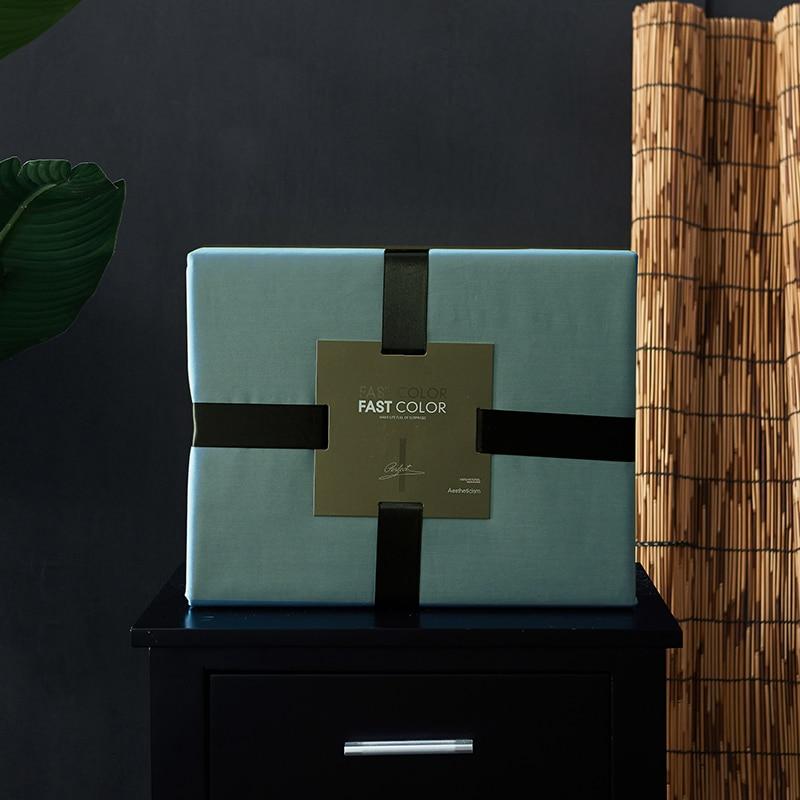 Decorative wrapped box with a black ribbon sitting on a black table next to a bamboo screen and a green leaf.