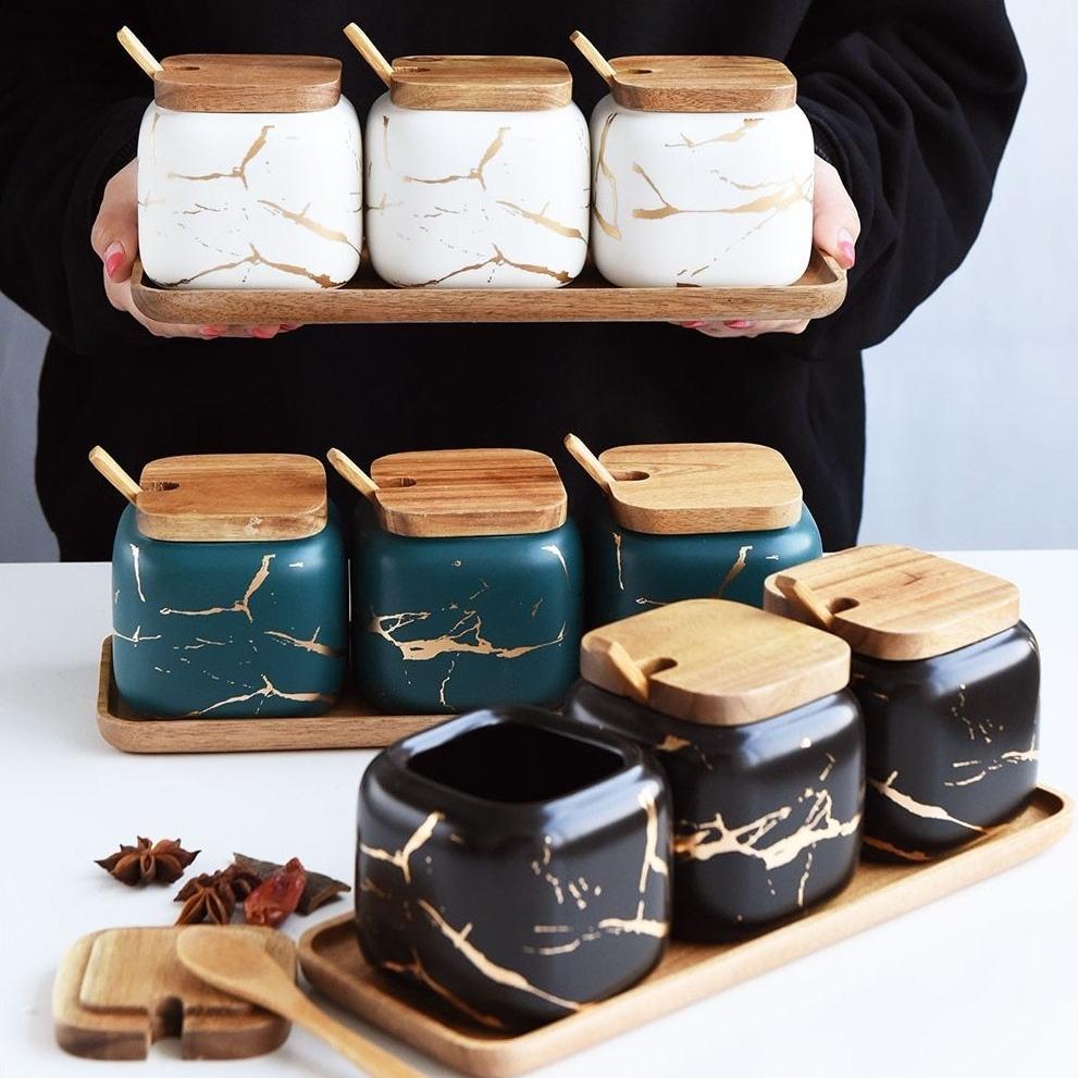 Maci 8-Piece Spice Ceramic Jar With Wooden Lid displayed on a table showcasing elegant marble patterns and wooden lids.