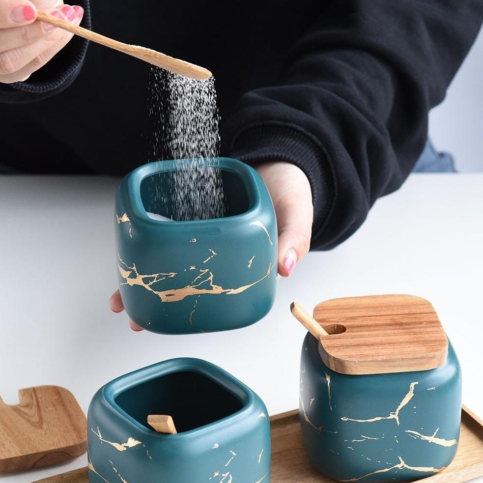 Person using spoon with Maci 8-Piece Spice Ceramic Jar With Wooden Lid for seasoning, highlighting the jar's elegant design.
