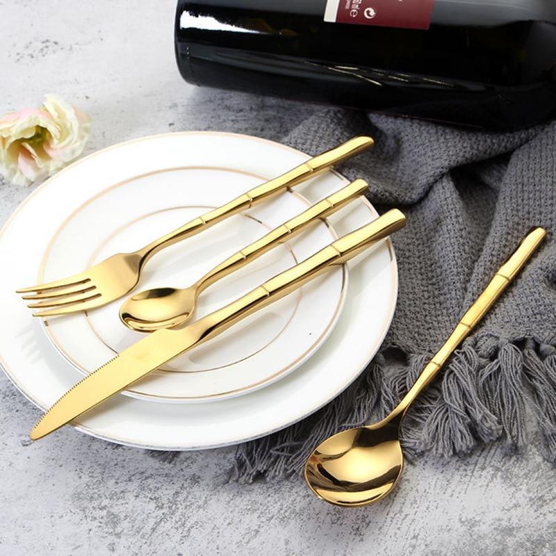 Lotus Flatware 24-Piece Set gold bamboo-style stainless steel cutlery on white plate with grey napkin, includes knife, fork, and spoon.