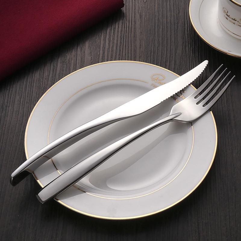 Talia Shiny Silver Flatware 24-Piece Set on gold-rimmed plate, showcasing elegant curved design and shiny polished silver finish.